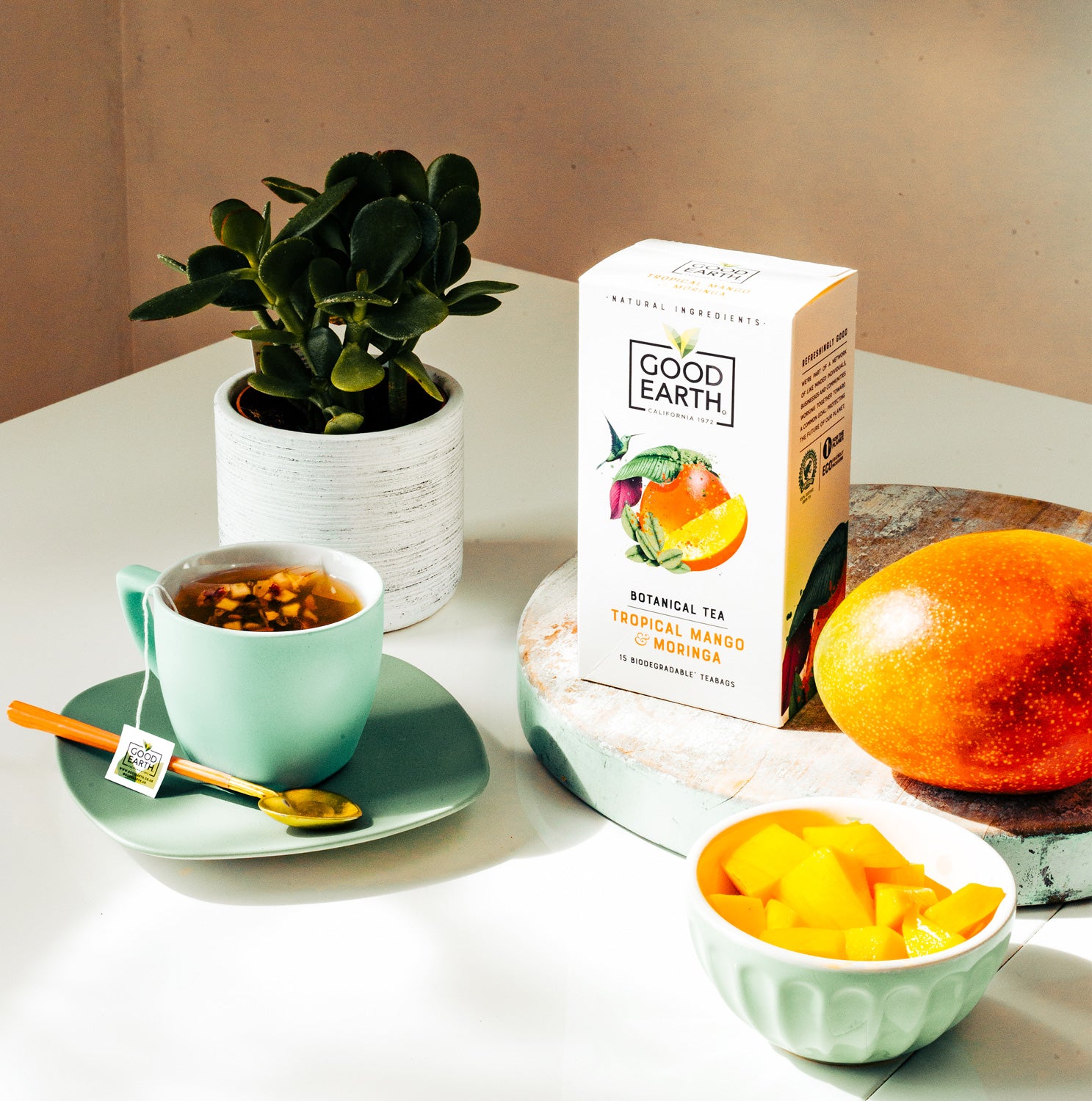 Good Earth Biodegradable Tea Bags image of a breakfast table with tea cup and tea packaging and mangoes